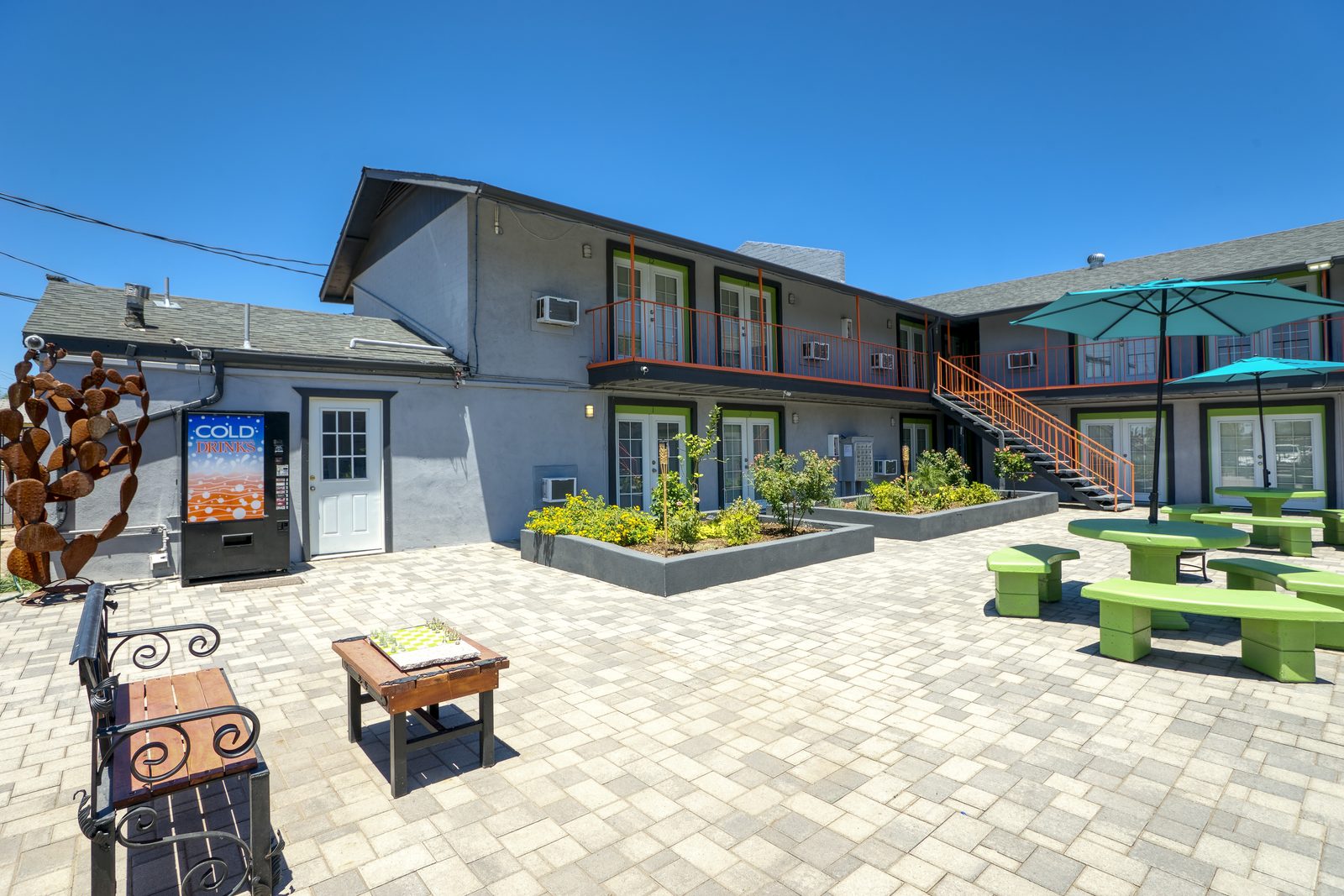 Lucky Star Flats courtyard with green picnic tables, umbrella, BBQ seating, and cold drinks vending machine