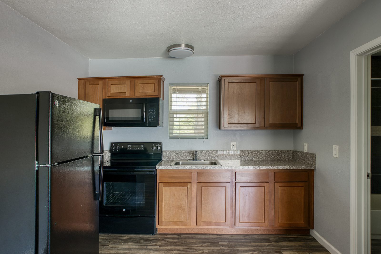 Remodeled kitchen with refrigerator, electric range, microwave, and granite countertops in Phoenix studio apartment