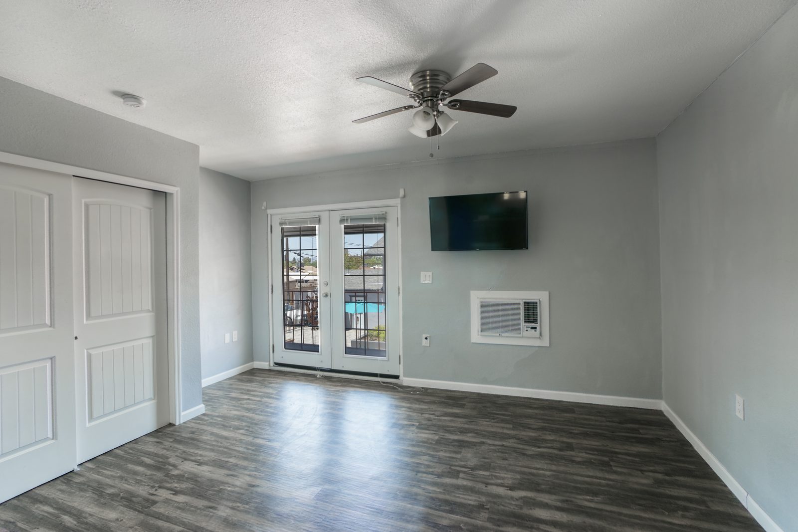 Studio apartment living area with mounted TV, in-unit A/C, ceiling fan, and french doors to balcony at Lucky Star Flats