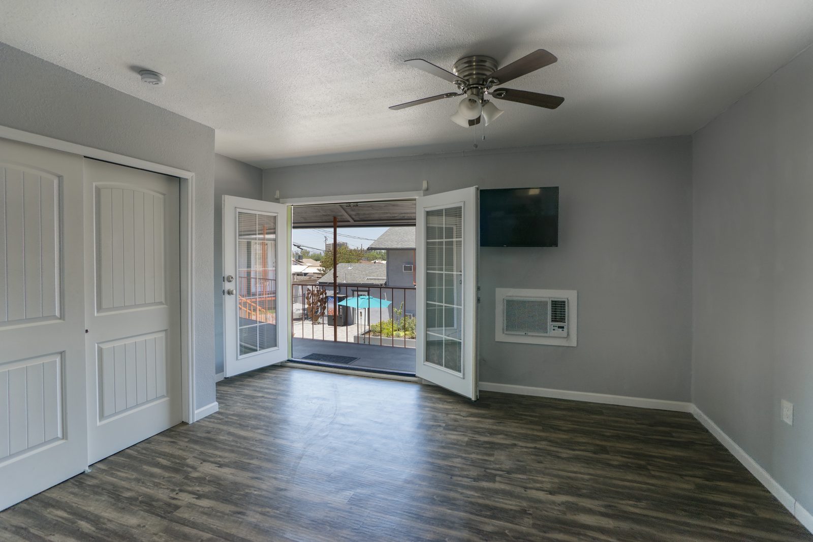 Studio apartment with french doors open to balcony and courtyard view, with mounted TV and A/C